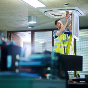 an HVAC specialist changes an air filter in an office ceiling