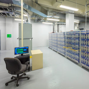 rows of machines that store data sit in a room with a solo desktop computer and chair